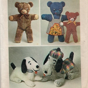 Pode incluir: Uma coleção de peluches incluindo três ursos de peluche e dois cães. Um urso castanho usa um laço xadrez, um urso azul usa um avental floral e um pequeno urso vermelho tem um laço amarelo. Um cão branco tem orelhas pretas e um cão cinzento usa um chapéu e um colete xadrez.