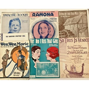 Könnte beinhalten: Eine Sammlung von Vintage-Notenblättern. Die Cover zeigen Illustrationen und Text, darunter Titel wie "Ramona", "Why Did I Kiss That Girl" und "So This Is Venice". Die Farbpalette umfasst Blau-, Rosa- und Brauntöne mit Porträts und Szenen.