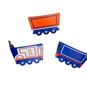 May include: Three blue and orange cardboard boxes shaped like train cars. The boxes are decorated with a train engine, a boxcar, and a caboose. The train engine has the number "1" on the side.