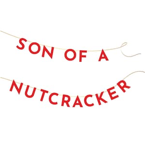 May include: Red paper banner with the text "SON OF A NUTCRACKER" strung on a gold string.