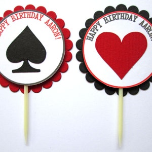 Peut inclure: Deux d&eacute;corations rondes pour cupcakes avec des bords festonn&eacute;s. Une d&eacute;coration a une pique noire et le texte "Happy Birthday Aaron!" L'autre d&eacute;coration a un c&oelig;ur rouge et le texte "Happy Birthday Aaron!"