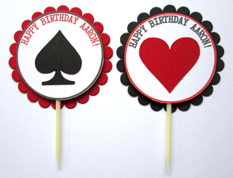 Peut inclure: Deux d&eacute;corations rondes pour cupcakes avec des bords festonn&eacute;s. Une d&eacute;coration a une pique noire et le texte "Happy Birthday Aaron!" L'autre d&eacute;coration a un c&oelig;ur rouge et le texte "Happy Birthday Aaron!"