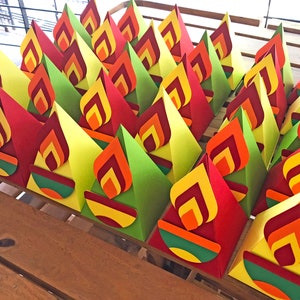 May include: A collection of colorful paper flame decorations. Each flame is made of layered red, orange, and yellow paper, with a green and orange base. The decorations are arranged on a wooden surface.
