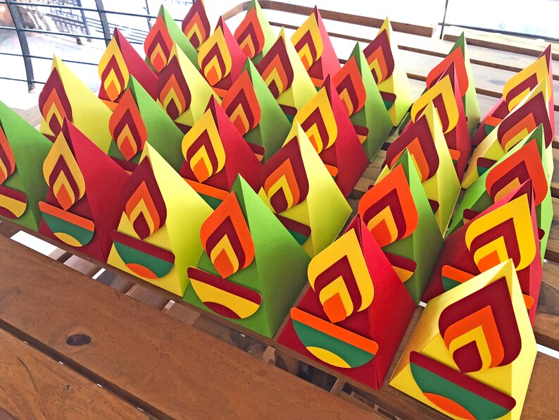 May include: A collection of colorful paper flame decorations. Each flame is made of layered red, orange, and yellow paper, with a green and orange base. The decorations are arranged on a wooden surface.