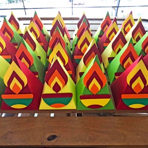 May include: A collection of colorful, cone-shaped paper decorations. Each cone features a flame design in shades of red, orange, and yellow, with a green and yellow base. The decorations are arranged on a wooden surface.