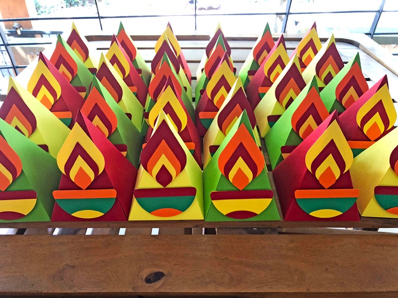May include: A collection of colorful, cone-shaped paper decorations. Each cone features a flame design in shades of red, orange, and yellow, with a green and yellow base. The decorations are arranged on a wooden surface.