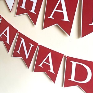 May include: Red and white banner with the text "Happy Canada" in white letters. The banner is made of paper and is strung together with red string.