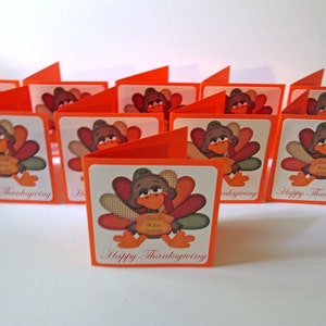 May include: A collection of Thanksgiving greeting cards. Each card features a cartoon turkey illustration with a brown head, colorful feathers, and orange feet. The cards are orange and white, with the text "Happy Thanksgiving".