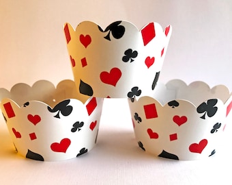 Könnte beinhalten: Drei weiße Cupcake-Förmchen mit gewelltem Rand. Jedes Förmchen ist mit Spielkartensymbolen in Rot und Schwarz verziert, darunter Herzen, Rauten, Kreuz und Pik. Die Förmchen sind gestapelt und leicht überlappend.