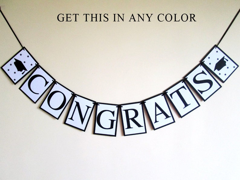 May include: A black and white banner with the word "CONGRATS" in large, bold letters. The banner is strung together with black string and has small black graduation caps with stars on each end.