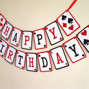 K&ouml;nnte beinhalten: Ein festliches Geburtstagsbanner aus Spielkarten-f&ouml;rmigen Ausschnitten. Jede Karte zeigt einen Buchstaben, der "HAPPY BIRTHDAY" in Rot und Schwarz auf wei&szlig;em Hintergrund schreibt. Die Karten sind mit einem roten Band verbunden.