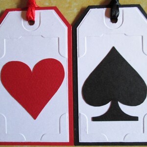 May include: Two white gift tags with red and black borders. The tag on the left has a red heart shape cut out. The tag on the right has a black spade shape cut out.