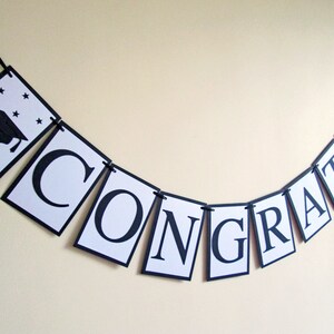 May include: Black and white graduation banner with the word "CONGRATS" and a graduation cap with stars on the first flag.