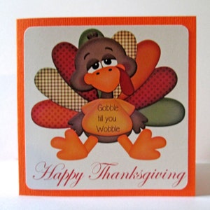 May include: Thanksgiving greeting card featuring a cartoon turkey with orange feet, beak, and wattle. The turkey has a brown body and colorful tail feathers. Text on the card reads "Gobble till you Wobble" and "Happy Thanksgiving."