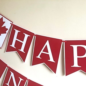 May include: Red and white banner with the words "HAPPY" in white letters on a red background. The banner is decorated with a red maple leaf on a white background.
