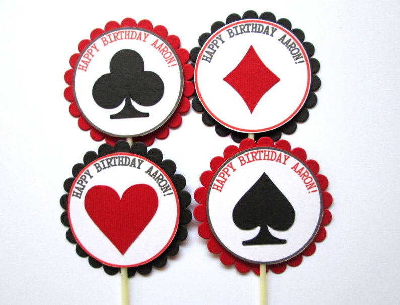 Peut inclure: Quatre d&eacute;corations rondes pour cupcakes avec des bords festonn&eacute;s noirs et des centres rouges. Chaque d&eacute;coration pr&eacute;sente une diff&eacute;rente carte de jeu : tr&egrave;fles, carreaux, c&oelig;urs et piques. Le texte "Happy Birthday Aaron!" est imprim&eacute; autour du bord de chaque d&eacute;coration.