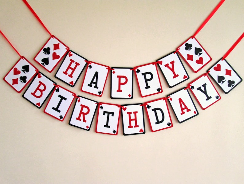 K&ouml;nnte beinhalten: Ein festliches Geburtstagsbanner aus Spielkarten-f&ouml;rmigen Karten. Jede Karte zeigt einen Buchstaben, der "HAPPY BIRTHDAY" in Schwarz und Rot schreibt, mit Kartensymbolen. Das Banner ist an einem roten Band befestigt.