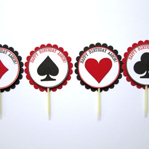 Peut inclure: Quatre d&eacute;corations rondes pour cupcakes avec des bords festonn&eacute;s noirs et des centres rouges. Chaque d&eacute;coration pr&eacute;sente une diff&eacute;rente carte &agrave; jouer : carreau, pique, c&oelig;ur et tr&egrave;fle. Le texte "Happy Birthday Aaron!" est imprim&eacute; en gris sur chaque d&eacute;coration.