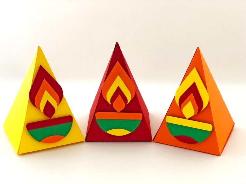May include: Three colorful, pyramid-shaped paper decorations. Each has a flame design in shades of red, orange, and yellow, above a green and yellow bowl shape. The pyramids are yellow, red, and orange.