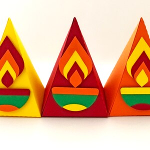 May include: Three colorful, pyramid-shaped paper decorations. Each has a flame design in shades of red, orange, and yellow, above a green, orange, and yellow bowl shape. The pyramids are yellow, red, and orange.