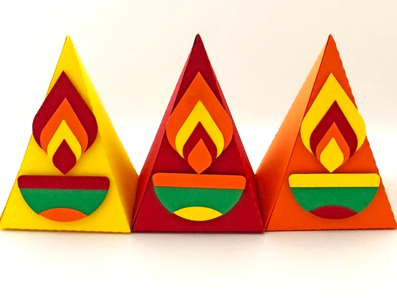 May include: Three colorful, pyramid-shaped paper decorations. Each has a flame design in shades of red, orange, and yellow, above a green, orange, and yellow bowl shape. The pyramids are yellow, red, and orange.