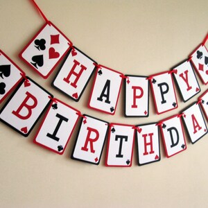 K&ouml;nnte beinhalten: Eine festliche Geburtstagsgirlande aus Spielkarten. Jede Karte zeigt einen Buchstaben, der "HAPPY BIRTHDAY" in Schwarz und Rot bildet. Die Karten sind mit einem roten Band verbunden, was eine verspielte Dekoration ergibt.