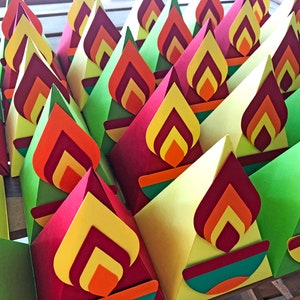 May include: A collection of colorful, cone-shaped paper decorations. Each cone features a layered flame design in shades of red, orange, and yellow. The cones are primarily red, yellow, and green, creating a vibrant display.