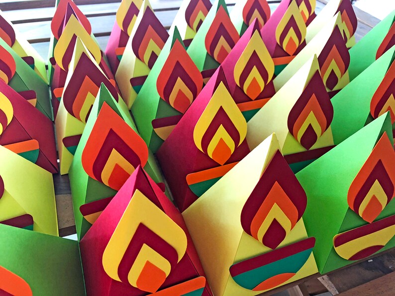May include: A collection of colorful, cone-shaped paper decorations. Each cone features a layered flame design in shades of red, orange, and yellow. The cones are primarily red, yellow, and green, creating a vibrant display.