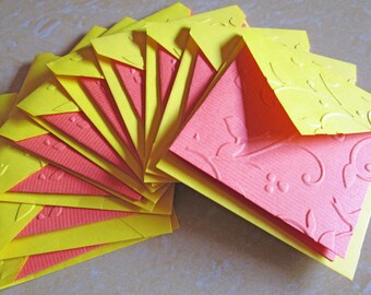 Pode incluir: Um conjunto de cartões de felicitações feitos à mão. Cada cartão apresenta uma camada externa amarela com desenhos florais em relevo e uma camada interna rosa, também em relevo. Os cartões estão dispostos em forma de leque.