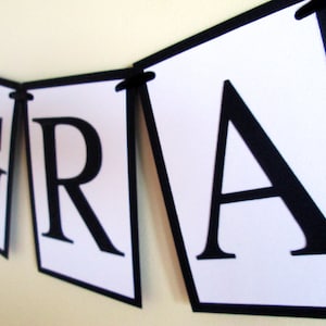 May include: Black and white banner with the word "GRAD" in large, bold letters. Each letter is on a separate white triangle with a black border.