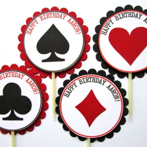 Peut inclure: Quatre d&eacute;corations rondes pour cupcakes avec des bords festonn&eacute;s rouges et noirs. Chaque d&eacute;coration pr&eacute;sente une diff&eacute;rente carte &agrave; jouer : pique, c&oelig;ur, tr&egrave;fle et carreau. Le texte "Happy Birthday Aaron!" est imprim&eacute; sur chaque d&eacute;coration.