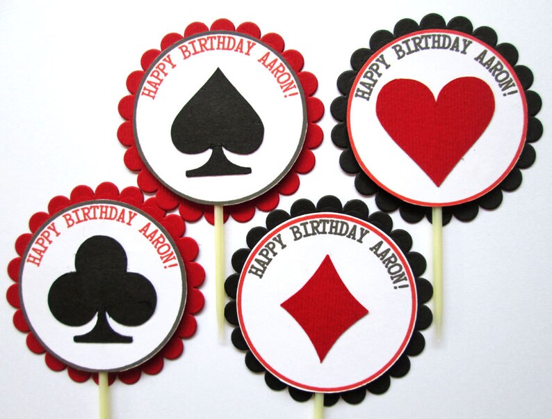 Peut inclure: Quatre d&eacute;corations rondes pour cupcakes avec des bords festonn&eacute;s rouges et noirs. Chaque d&eacute;coration pr&eacute;sente une diff&eacute;rente carte &agrave; jouer : pique, c&oelig;ur, tr&egrave;fle et carreau. Le texte "Happy Birthday Aaron!" est imprim&eacute; sur chaque d&eacute;coration.