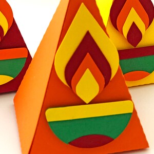 May include: Close-up of three colorful, pyramid-shaped paper decorations. Each pyramid features a flame design in yellow, orange, and red, above a green and yellow bowl shape. The pyramids are orange, red, and yellow.