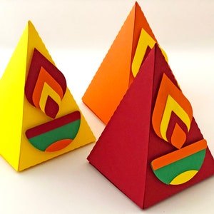 May include: Three colorful, pyramid-shaped paper decorations. Each has a flame design in shades of red, orange, and yellow. The base of each pyramid features a green and orange design. One is yellow, one is orange, and one is red.