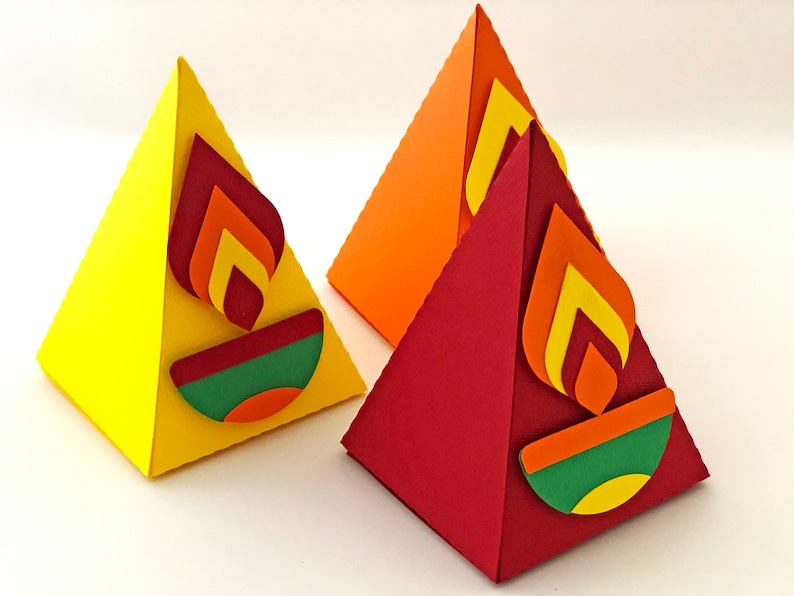 May include: Three colorful, pyramid-shaped paper decorations. Each has a flame design in shades of red, orange, and yellow. The base of each pyramid features a green and orange design. One is yellow, one is orange, and one is red.
