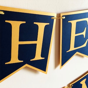 May include: A navy blue banner with gold lettering spelling out a word. The banner is made of individual pennant-shaped flags with gold trim and strung together with gold string. The letters are large and easy to read.