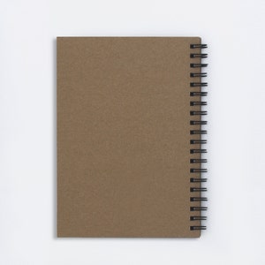 Puede incluir: Un cuaderno de espiral marr&oacute;n con una portada en blanco.