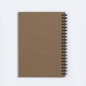 May include: A brown spiral-bound notebook with a textured cover. The notebook's pages are held together by a black metal spiral binding along the left edge. The cover is a solid, neutral brown color.