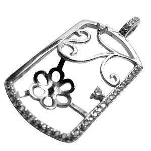 May include: A silver pendant with a rectangular frame, adorned with a floral design and small, sparkling stones. The pendant features a decorative openwork pattern and a loop for a chain.