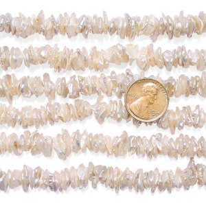 May include: Close-up of strands of off-white, irregular freshwater pearls. A penny is included for size reference. The pearls have a natural, organic appearance, suitable for jewellery making. The pearls are strung together, ready for necklaces or bracelets.
