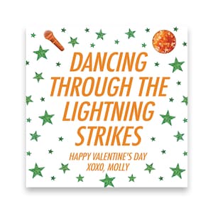 May include: Square white card with orange text that reads "Dancing Through The Lightning Strikes." The card has green glitter stars and illustrations of a microphone and a disco ball. The text "Happy Valentine's Day XOXO, Molly" is also included.