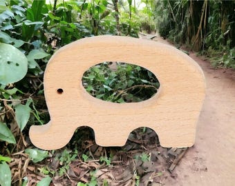 May include: A light brown wooden cutout in the shape of an elephant with a smooth, natural grain finish. The figure features a large oval cutout in the center representing the body and a small circular hole serving as the eye of the elephant.