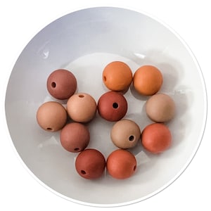 May include: A collection of ten round silicone beads in various shades of brown, beige, and terracotta. The beads are arranged in a bowl.