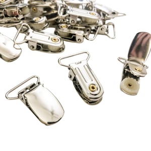 May include: A close-up of silver metal suspender clips. The clips have a smooth, shiny finish and are designed to attach to clothing.