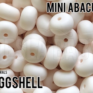 May include: A close-up image of a pile of small, off-white silicone beads with a hole in the center. The beads are arranged in a random pattern. The text "MINI ABACUS" is at the top of the image and the text "NEUTRALS EGGSHELL" is at the bottom of the image.