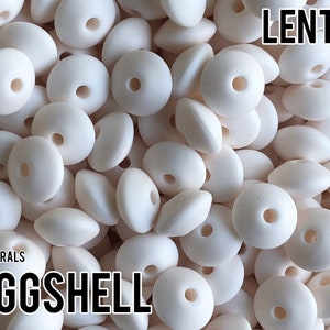 May include: A close-up of a pile of white lentil-shaped silicone beads. The beads have a hole in the center and are arranged in a random pattern. The text "LENTIL" and "EGGSHELL" are visible in the image.