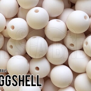 May include: A close-up image of a pile of eggshell-colored silicone beads. The beads are round and have a hole in the center. The beads are used for making jewelry or other crafts.
