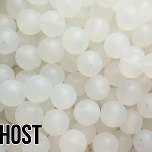 May include: A close-up of a large quantity of white, opaque, round beads. The beads are arranged in a random pattern and appear to be made of plastic.