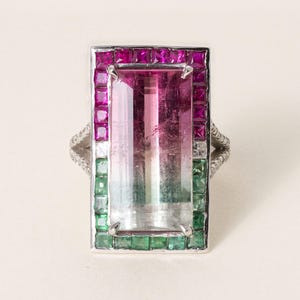 Peut inclure: Une bague rectangulaire en argent ornée d'une grande tourmaline bicolore allongée passant du rose au vert. La pierre centrale est entourée d'une bordure de petits rubis roses et d'émeraudes vertes taillés en carré, avec des diamants pavés sur l'anneau.