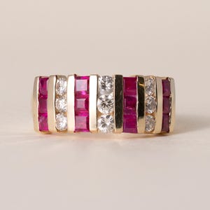 Puede incluir: Un anillo de oro con filas alternas de rubíes cuadrados y piedras preciosas claras. El anillo tiene una banda de oro y está engastado con múltiples piedras preciosas. Las piedras preciosas están dispuestas en un patrón repetitivo.
